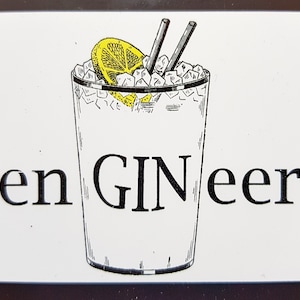 Könnte beinhalten: Ein weißes Schild mit schwarzem Text, der "en GINeer" lautet, und einer Schwarzweißillustration eines Gin-Glases mit Eis und einer Zitronenscheibe.