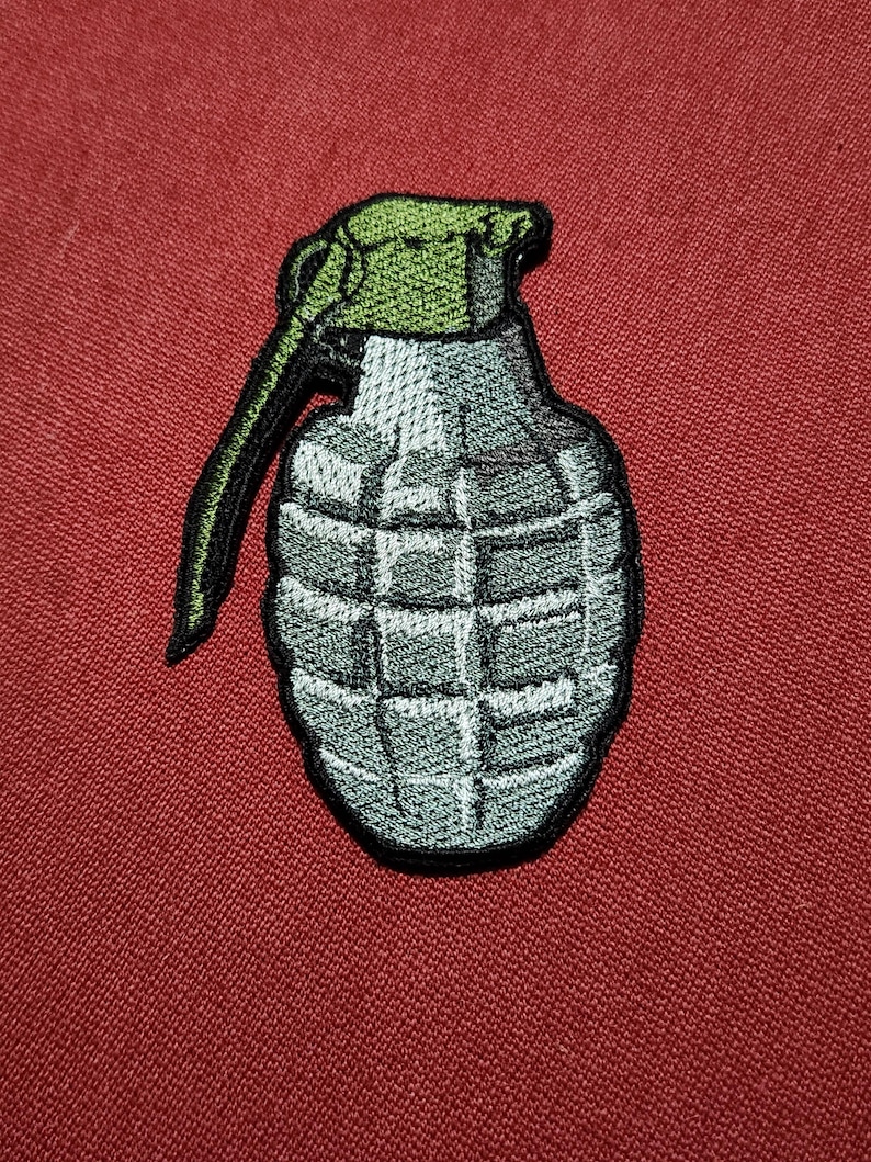 Op de afbeelding: Geborduurde patch van een grijze handgranaat met een groene bovenkant en zwarte trekpen. De patch staat op een rode achtergrond. De granaat heeft een gedetailleerd, gestructureerd ontwerp.