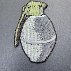 May include: Embroidered patch in the shape of a hand grenade. The patch features a grey and black body with a light green top and pull pin. The patch is outlined in black.