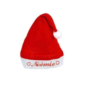 Peut inclure: Un bonnet de Père Noël rouge avec une bordure blanche et un pompon blanc. Le nom "Noémie" est brodé en cursive sur la bordure blanche. Le chapeau est en matière douce et pelucheuse.