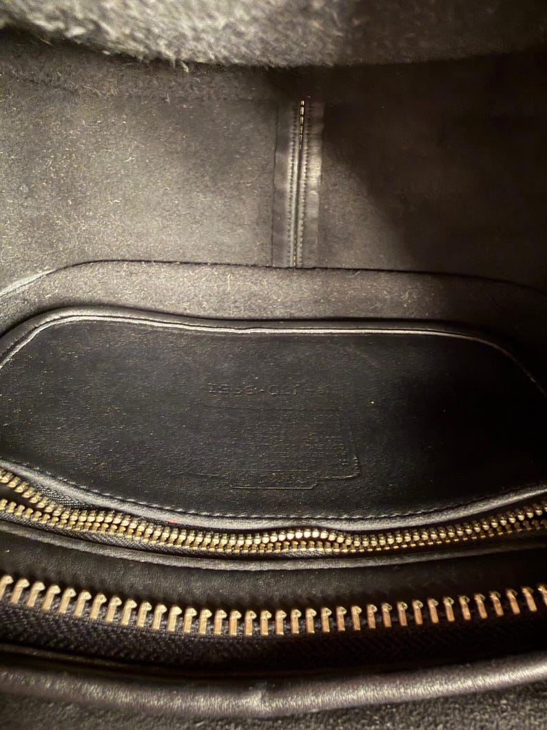 May include: Black leather handbag interior with a gold zipper and a small leather pocket. The interior is lined with a soft, dark material. The bag appears to be well-worn.