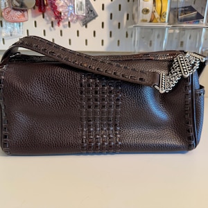 May include: A dark brown leather handbag with a woven center panel and a decorative silver chain accent. The bag has a top handle and a long strap for shoulder or crossbody wear. The leather has a textured appearance.