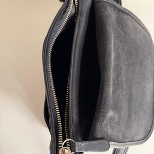 May include: Black leather shoulder bag with silver-tone hardware. The bag features a top handle, a shoulder strap, and multiple compartments. The main compartment is open, revealing the interior. The bag has a zipper closure and a flap closure.