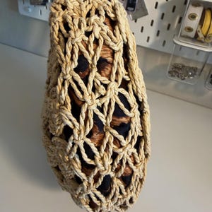 Op de afbeelding: Een beige geweven tas met een bruin lederen handvat. De tas heeft een netachtig ontwerp, dat een voering van luipaardprintstof onthult. De tas wordt door een hand vastgehouden, wat de textuur en stijl van het accessoire laat zien.
