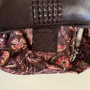 May include: A dark brown leather handbag with a woven top detail. The interior lining features a floral pattern in shades of pink, yellow, and white against a dark brown background. A leather tag is visible inside.