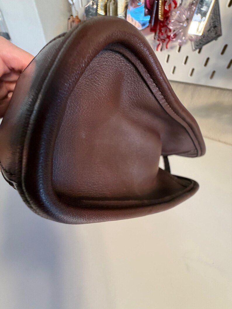 May include: A dark brown leather handbag, showcasing a curved, structured design. The bag's surface has a textured appearance, with visible stitching along the edges. The image highlights the bag's shape and material.