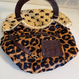 Op de afbeelding: Een handtas met luipaardprint met een bruin handvat en een geweven beige bovenkant. De tas heeft een bruin lederen accent met het woord "Brighton" in reli&euml;f. Een kleine bruine riem met een gouden sluiting is aan de tas bevestigd.