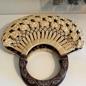 Op de afbeelding: Een beige en bruine handtas met een ronde handgreep. De tas heeft een geweven ontwerp met een luipaardprint voering. De handgreep is bruin met witte stiksels en een bladerenpatroon.