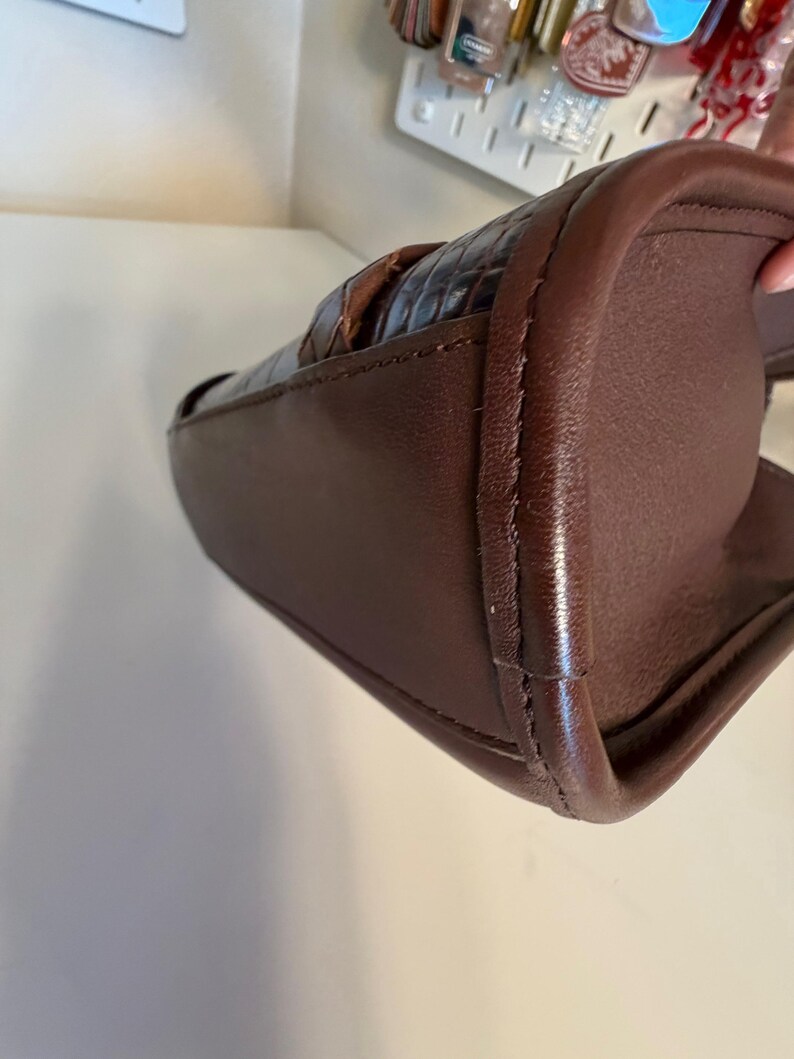 May include: A brown leather handbag with a woven top section. The bag has a rectangular shape with rounded corners and a stitched seam detail. The leather appears to be a rich, dark brown color.