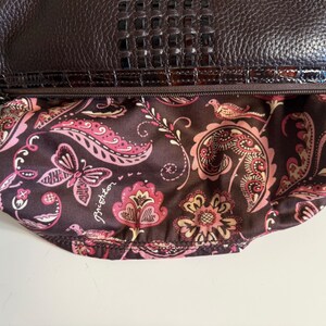 May include: A dark brown leather handbag with a textured top flap and a patterned interior. The interior fabric features a paisley design with pink and cream-colored floral and butterfly motifs. The bag has a silver chain strap.