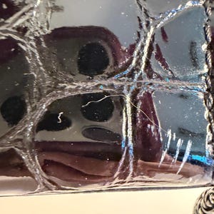 Puede incluir: Primer plano de un bolso negro brillante y texturizado. La superficie tiene un patr&oacute;n acolchado con costuras visibles. Una cadena plateada y un dije decorativo son visibles en el lateral. El bolso refleja la luz.