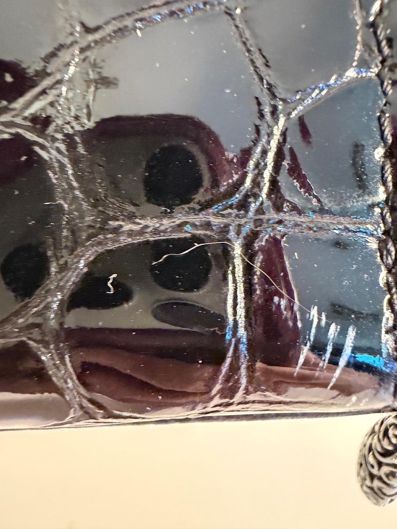 Puede incluir: Primer plano de un bolso negro brillante y texturizado. La superficie tiene un patr&oacute;n acolchado con costuras visibles. Una cadena plateada y un dije decorativo son visibles en el lateral. El bolso refleja la luz.