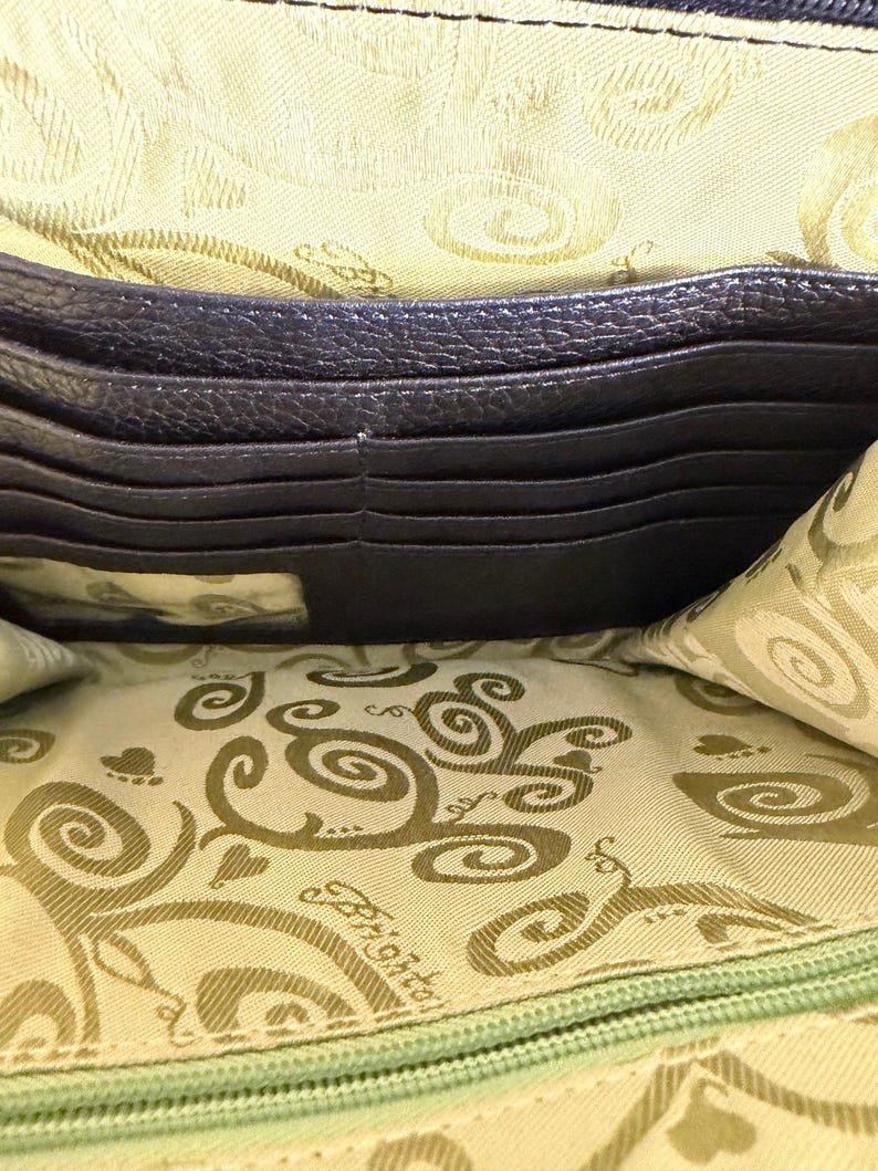Puede incluir: Vista abierta de una cartera de cuero marr&oacute;n oscuro, que revela m&uacute;ltiples ranuras para tarjetas y un forro interior estampado. El forro presenta un dise&ntilde;o repetitivo de espirales y el nombre de la marca. La cartera est&aacute; abierta, mostrando su organizaci&oacute;n interna.