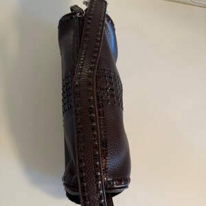 May include: A dark brown leather handbag with a woven design on the lower portion and a textured leather strap. The bag has a zipper closure and silver-colored hardware.