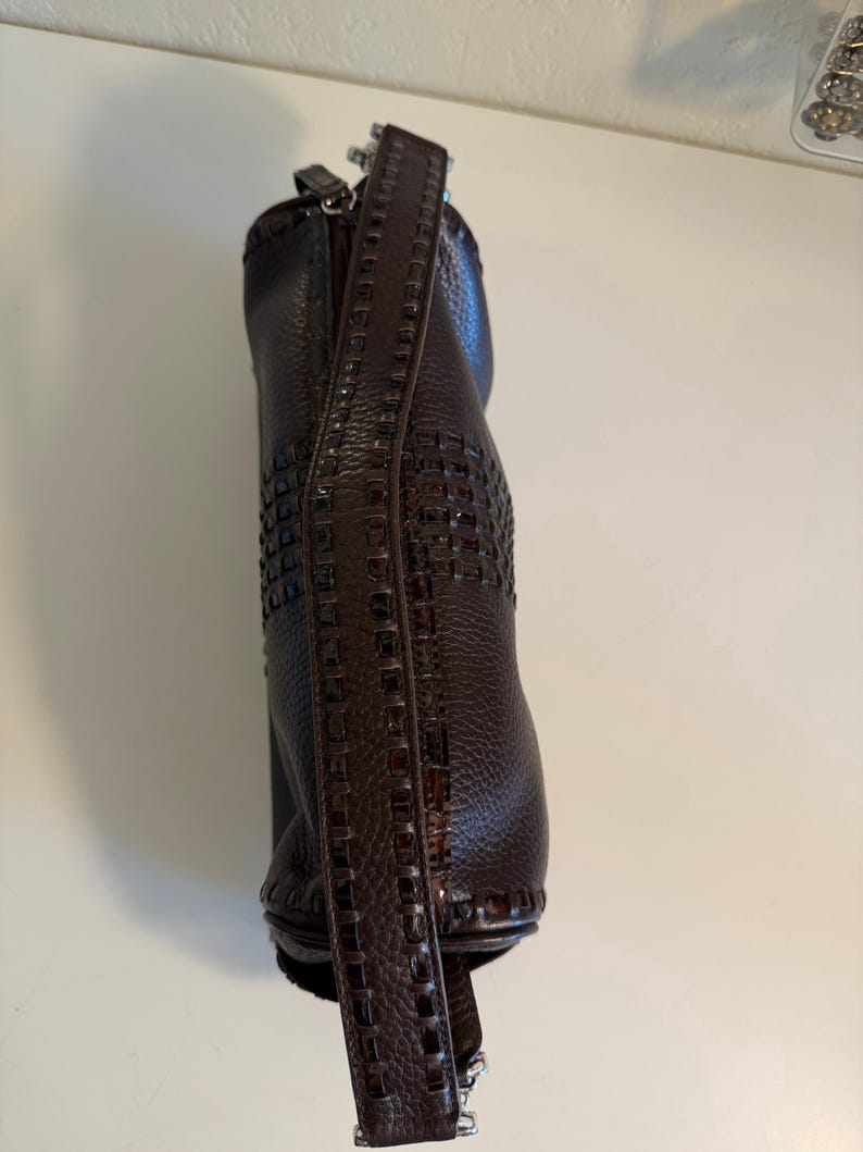 May include: A dark brown leather handbag with a woven design on the lower portion and a textured leather strap. The bag has a zipper closure and silver-colored hardware.