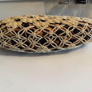 Op de afbeelding: Een beige, ovale clutch met een geweven, opengewerkt ontwerp. De binnenstof heeft een bruine en zwarte dierenprint. De tas ligt op een wit oppervlak.