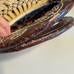 Op de afbeelding: Een vintage handtas met een geweven stro en haakontwerp. De tas heeft een bruin lederen handvat met witte stiksels. De binnenvoering heeft een luipaardprint. De tas is open en onthult de binnenkant.