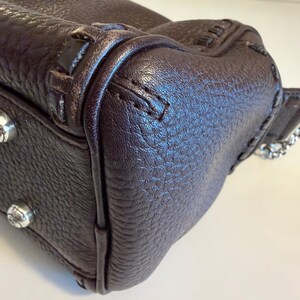 May include: Close-up of a dark brown leather handbag. The bag features a textured surface, visible stitching, and silver-toned hardware. The corner of the bag is visible, showcasing the craftsmanship and design details.