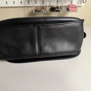 May include: A black leather handbag with a rounded shape. The bag has a structured design with visible stitching and a smooth, polished surface. The bottom of the bag is slightly curved.