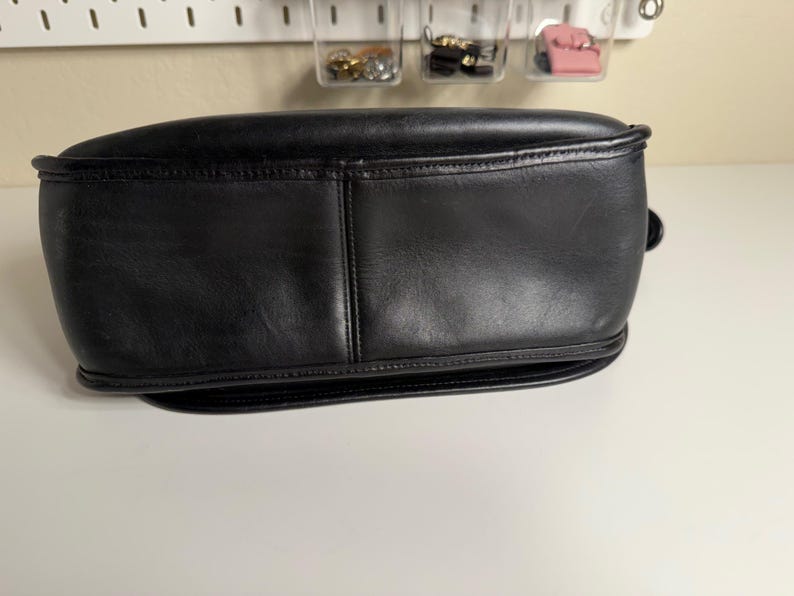 May include: A black leather handbag with a rounded shape. The bag has a structured design with visible stitching and a smooth, polished surface. The bottom of the bag is slightly curved.