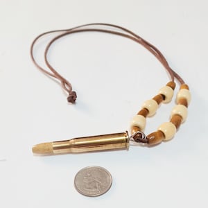 May include: A brown leather cord necklace with a brass bullet pendant and wooden beads. The beads are a mix of light brown and cream.