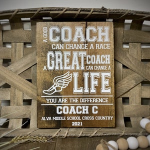 May include: A wooden sign with the text "A good coach can change a race. A great coach can change a life. You are the difference. Coach C. Alva Middle School Cross Country 2021."