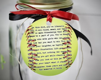 May include: A yellow softball with red stitching and a white background. The softball has a quote about the memories of playing softball on it. The quote reads: "On this dirt, you've literally left it all-blood, sweat, and tears. You've made friendships that will always be a part of you. You've fought side by side with girls who can relate with how bad you want to win. This dirt holds your laughter, as tightly as it holds your frustration. Life goes on off, of this dirt, but nothing can compare to the feeling you get while standing on it. Each time you look at this jar of dirt, know in your heart what it stands for and remember these years and all of the memories it holds."