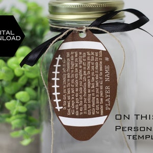 May include: A brown football-shaped tag with white stitching and text that reads "On this dirt, you've literally left it all - blood, sweat, and tears. You've made friendships that will always be a part of you. You've fought side by side with guys who can relate with how bad you want to win. This dirt holds your laughter, as tightly as it holds your frustration. Life goes on off of this dirt, but nothing can compare to the feeling you get while standing on it. Each time you look at this jar of dirt, know in your heart what it stands for and remember these years and all of the memories it holds. PLAYER NAME #"  The tag is tied to a clear glass jar with a black ribbon.