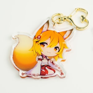 Può includere: Un portachiavi in acrilico trasparente con un personaggio dei cartoni animati con capelli arancioni, un kimono bianco e rosso e una grande coda arancione. Il personaggio sorride e ha un'espressione giocosa. Il portachiavi ha un anello in metallo dorato a forma di cuore.