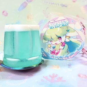 May include: A glass of blue jelly with a white top sits on a spoon. A round package with a cartoon character and the text "SUISEN'S SEA SALT JELLY" is next to it. The package also says "salty and sweet".