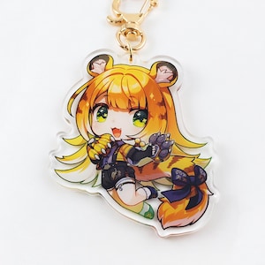 May include: A clear acrylic keychain featuring a cartoon character with yellow hair and tiger-like features. The character is wearing a black outfit with a purple bow and holding a ball. The keychain has a gold-colored clasp.