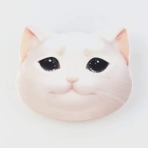 Puede incluir: Una pegatina blanca con forma de gato con una expresión triste. El gato tiene ojos grandes y negros y una boca ligeramente hacia abajo, lo que le da una apariencia melancólica. La pegatina probablemente está hecha de papel o un material similar.