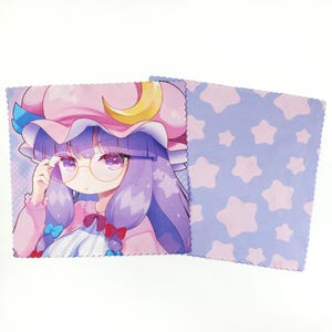 Könnte beinhalten: Zwei Mikrofasertücher. Eines zeigt ein Cartoon-Mädchen mit lila Haaren, Brille und einem rosa Hut mit gelbem Halbmond. Das andere Tuch hat einen hellblauen Hintergrund mit rosa Sternen. Beide Tücher haben einen gewellten Rand.