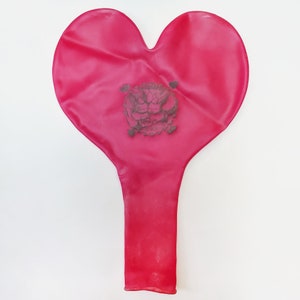 May include: A red heart-shaped balloon with a black and white design of two cartoon characters holding hands.