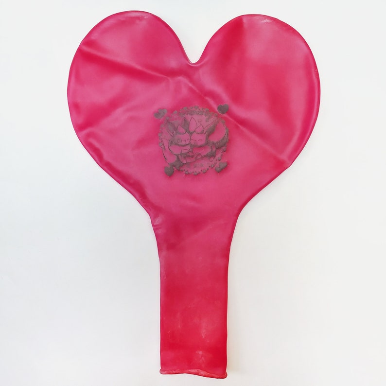 May include: A red heart-shaped balloon with a black and white design of two cartoon characters holding hands.