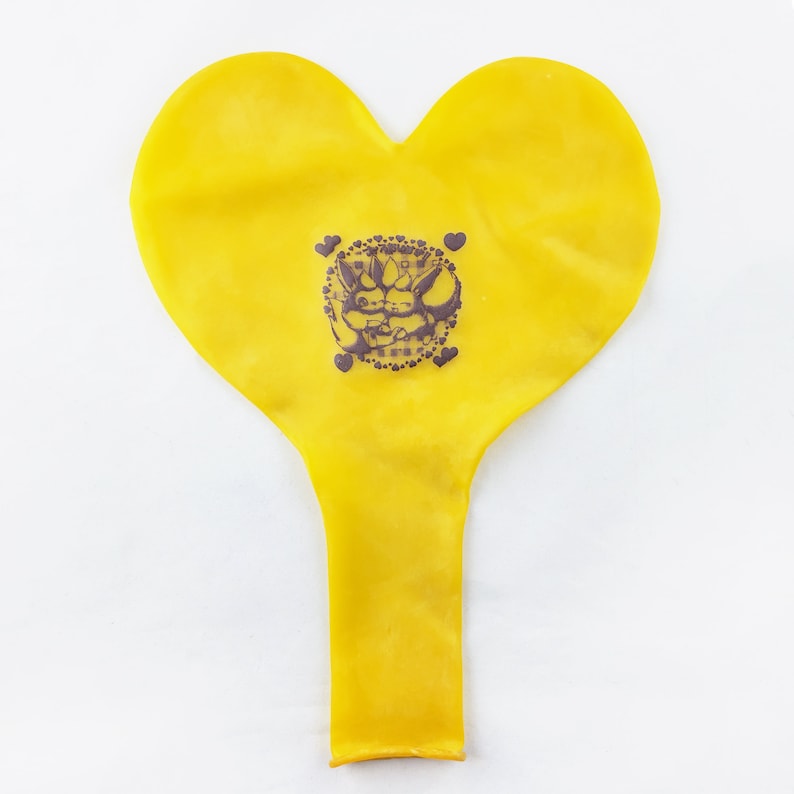 May include: A yellow heart-shaped balloon with a black and white graphic of two cartoon characters hugging. The graphic is surrounded by a circle of small hearts.