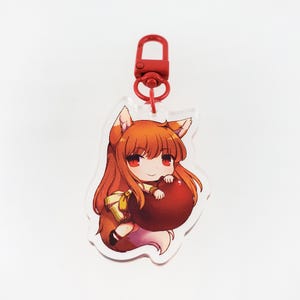 May include: A red and white anime character keychain with a red heart. The character has long orange hair and is wearing a yellow and white dress.