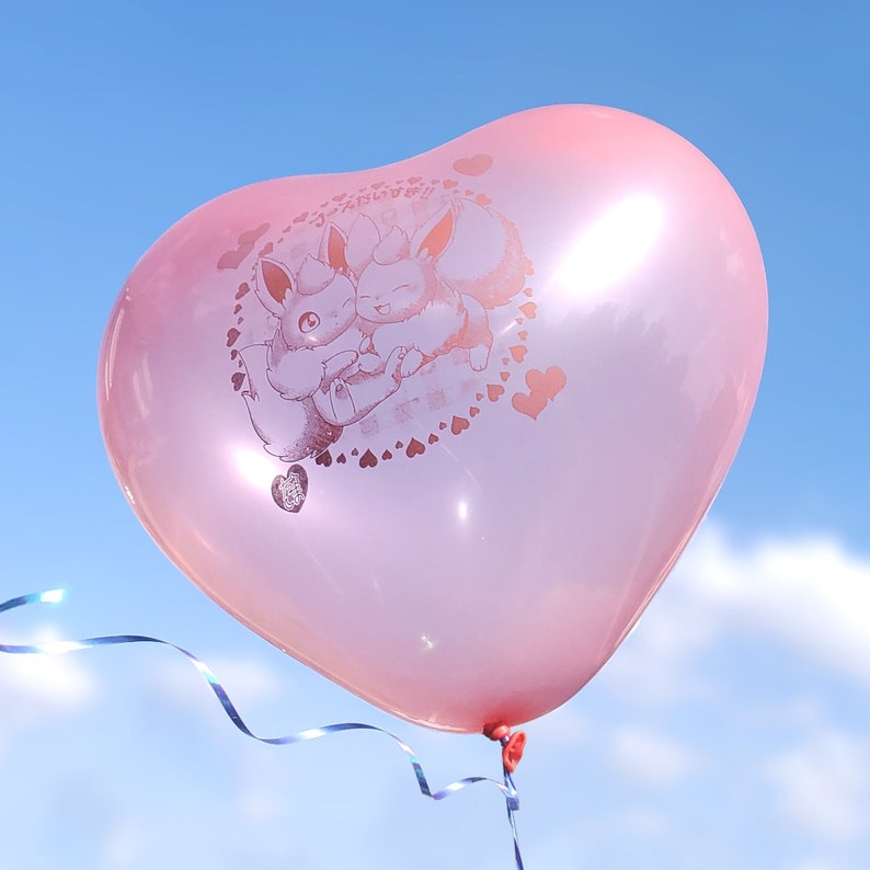 May include: A pink heart-shaped balloon with a graphic of two cartoon Pokemon characters, Eevee and Flareon, hugging. The balloon has the text "みんな大好き！" printed on it.