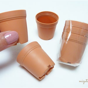 Pode incluir: Um conjunto de seis vasos de plantas de plástico na cor terracota. Os vasos são pequenos e embalados em um saco de plástico transparente. Os vasos são ideais para iniciar sementes ou propagar plantas.
