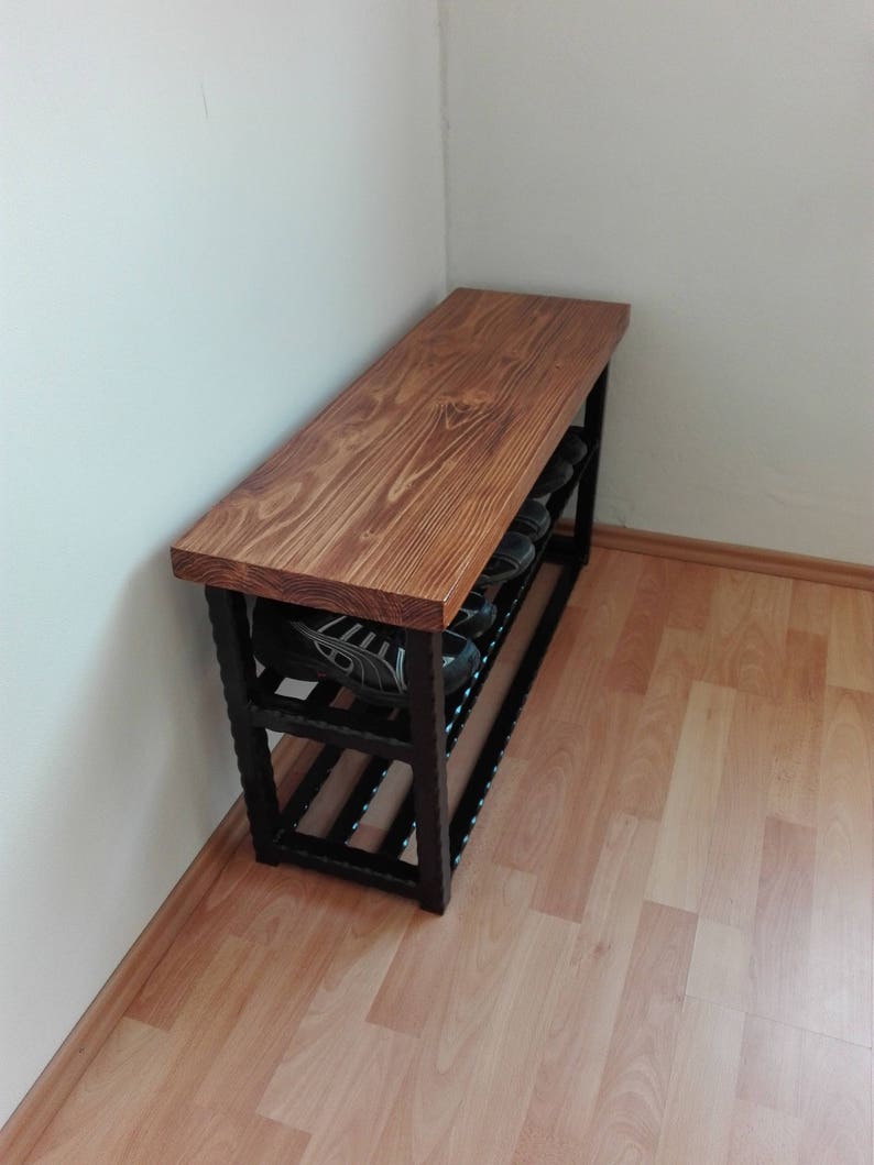May include: A wooden shoe bench with a dark brown stained top and a black metal frame. The bench has two shelves for shoe storage and is placed against a white wall. The bench is approximately 48 inches long.