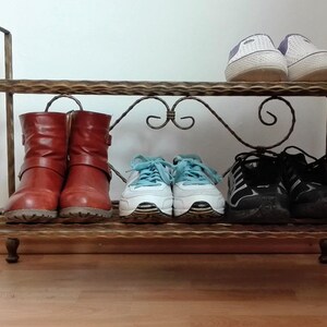 May include: A metal shoe rack with two shelves. The top shelf has two pairs of white sneakers and the bottom shelf has two pairs of brown boots and two pairs of black sneakers.