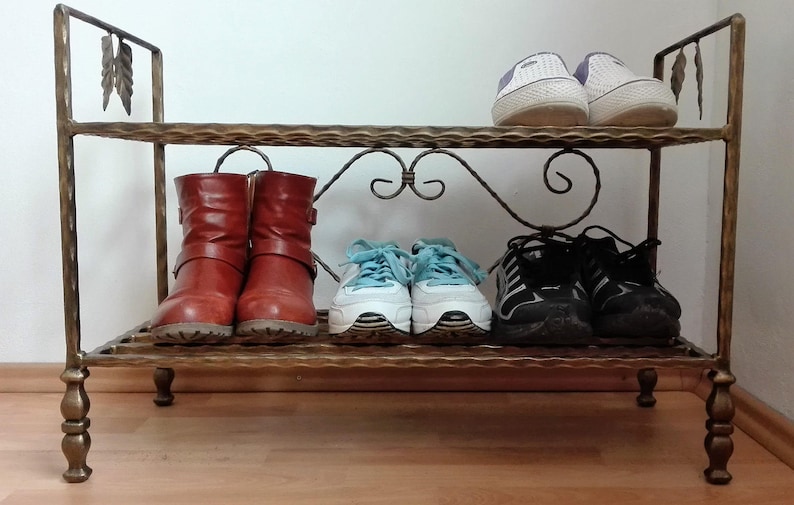 May include: A metal shoe rack with two shelves. The top shelf has two pairs of white sneakers and the bottom shelf has two pairs of brown boots and two pairs of black sneakers.