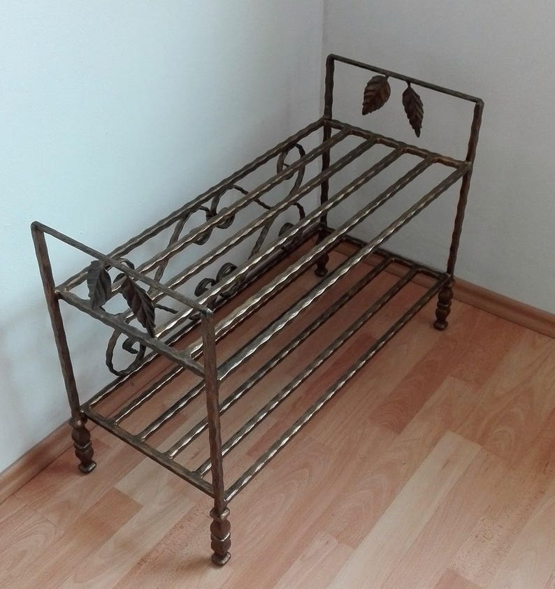 May include: A two-tiered metal shoe rack with a decorative scrolled design and leaf accents. The rack is made of wrought iron and has a gold finish.