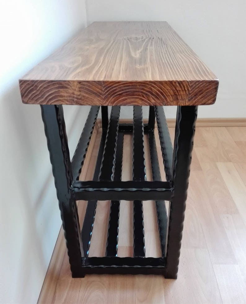 May include: A wooden bench with a natural finish and a black metal frame. The bench has a rectangular top and a lower shelf. The frame is made of vertical and horizontal bars. The bench is approximately 48 inches long.