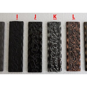 May include: A collection of eight rectangular decorative panels with embossed floral designs. The panels vary in color, including shades of gray, black, bronze, and white. Each panel is approximately 1 inch wide and 4 inches long.