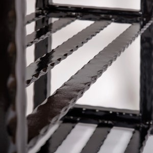 May include: Close-up of a black metal shelf with a textured, hammered finish. The shelf has multiple levels with horizontal bars and vertical supports. The design is industrial and modern, with a focus on the texture and the dark color.