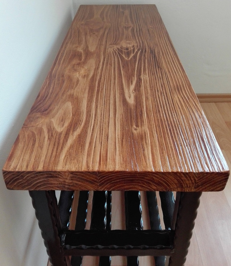 May include: A wooden bench with a stained, light brown top and a dark brown, decorative base. The bench top has visible wood grain and a textured surface. The base features vertical, dark brown supports.