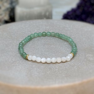 Pode incluir: Um bracelete de contas verdes e brancas com detalhes dourados. O bracelete é feito com contas de aventurina verde e pedra da lua.