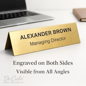 May include: A gold-colored desk nameplate with the name "ALEXANDER BROWN" and title "Managing Director" in black lettering. The nameplate is engraved on both sides and visible from all angles. The De Cube Basics Reimagined logo is in the bottom left.