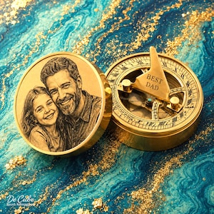 May include: A gold compass with a hinged lid, displaying a portrait of a father and child. The compass dial is engraved with Roman numerals and the words "BEST DAD". The background is a blue and gold marbled design.